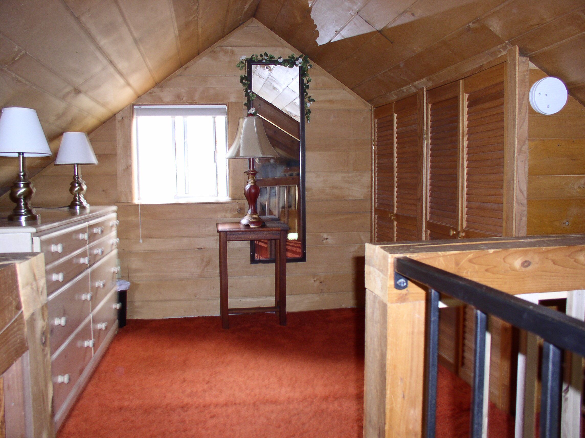 Un intérieur en bois avec un escalier, une commode avec des lampes et une fenêtre.