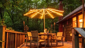 A wooden deck with a table and chairs, surrounded by a wooden fence and trees.