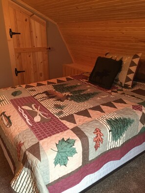 Une chambre avec un plafond en bois, un lit recouvert d’une courtepointe à motifs et une armoire en bois.