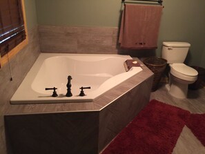 Une salle de bain avec une grande baignoire, des toilettes et un tapis rouge.