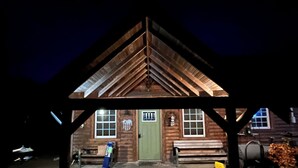 Una cabaña de madera con techo empinado, una puerta verde y una ventana con diseño de cuadrícula.