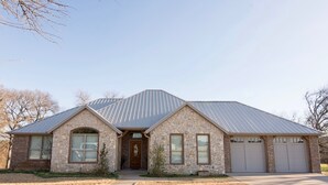Une maison en pierre à deux étages, avec un toit en métal, une porte d’entrée et deux portes de garage.