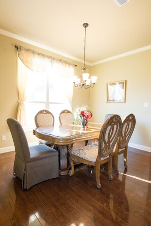 A dining room with a wooden table, four chairs, a chandelier, and a vase with flowers.