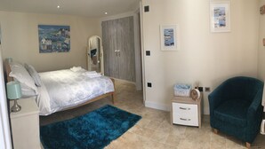 Un dormitorio con cama, una alfombra azul, una mesita de noche con lámpara, una silla y obras de arte en las paredes.