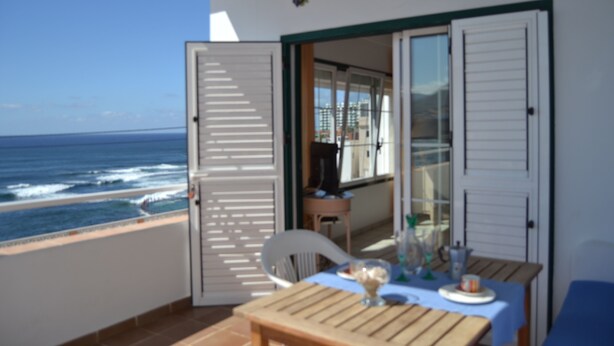Een balkon met een tafel en stoelen, met uitzicht op de oceaan.