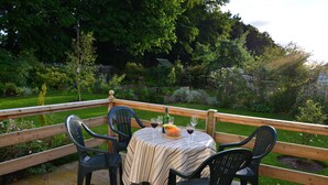 An outdoor deck with a table set for dining, surrounded by chairs, overlooking a lush garden.