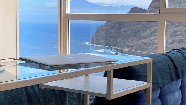 A modern room with a glass desk, a laptop, and a view of the ocean and mountains. - Casa Julietta - comfortable and spacious home with the BEST VIEWS in La Gomera (Hermigua)