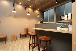 Un coin bar accueillant avec des tabourets en bois, un tableau noir où sont écrits des messages et une étagère avec des tasses et des condiments.