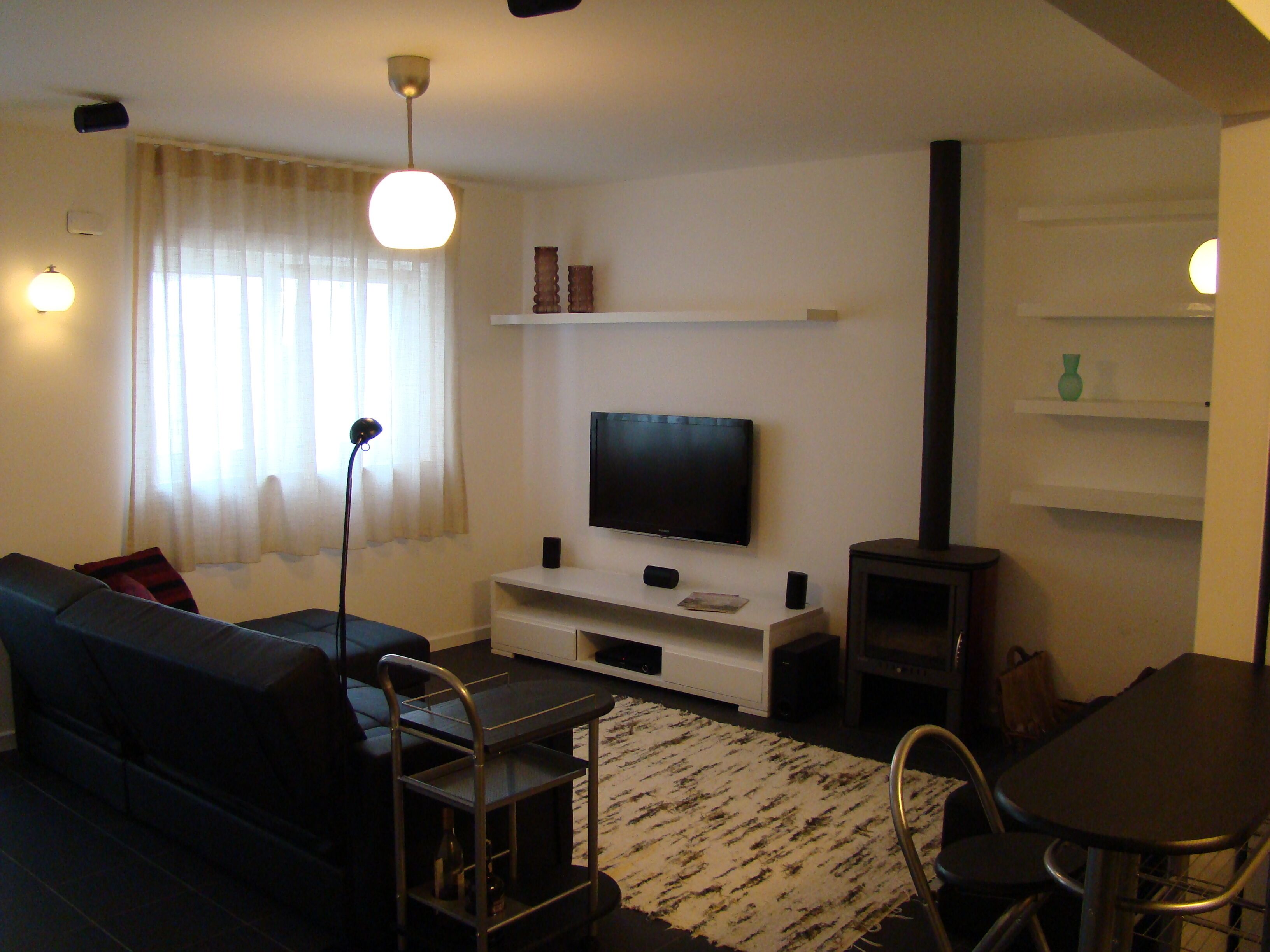 A living room with a sofa, TV, entertainment unit, and a small dining area with a table and chairs.