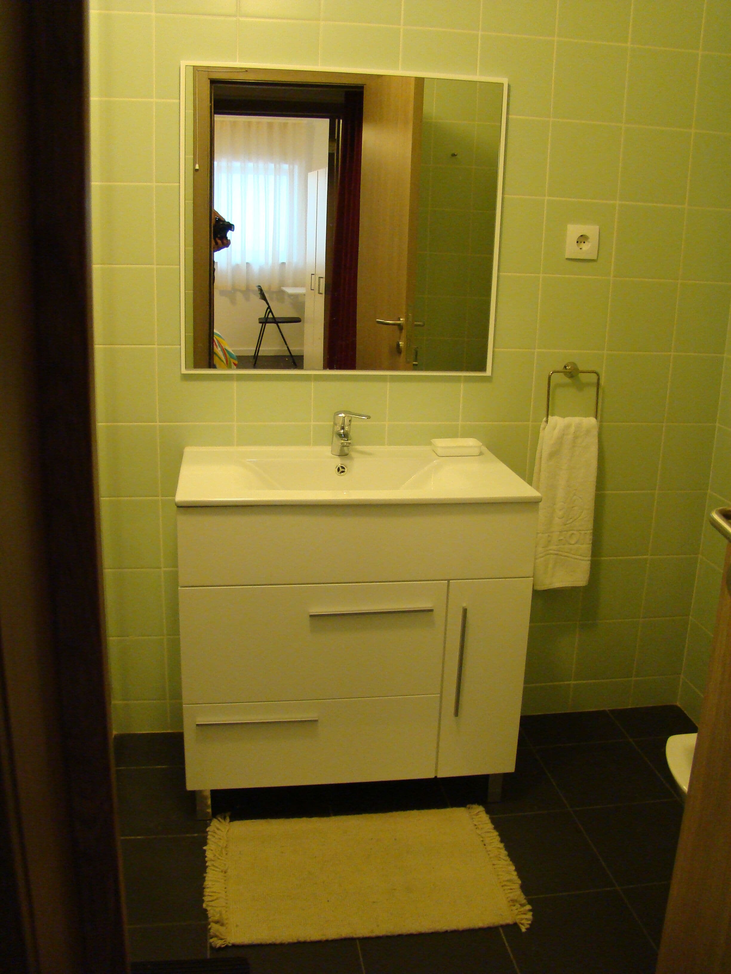 Un baño con un lavamanos blanco, un espejo y un perchero para toallas.
