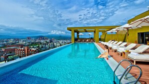 A rooftop infinity pool with a city view, lounge chairs, and umbrellas.