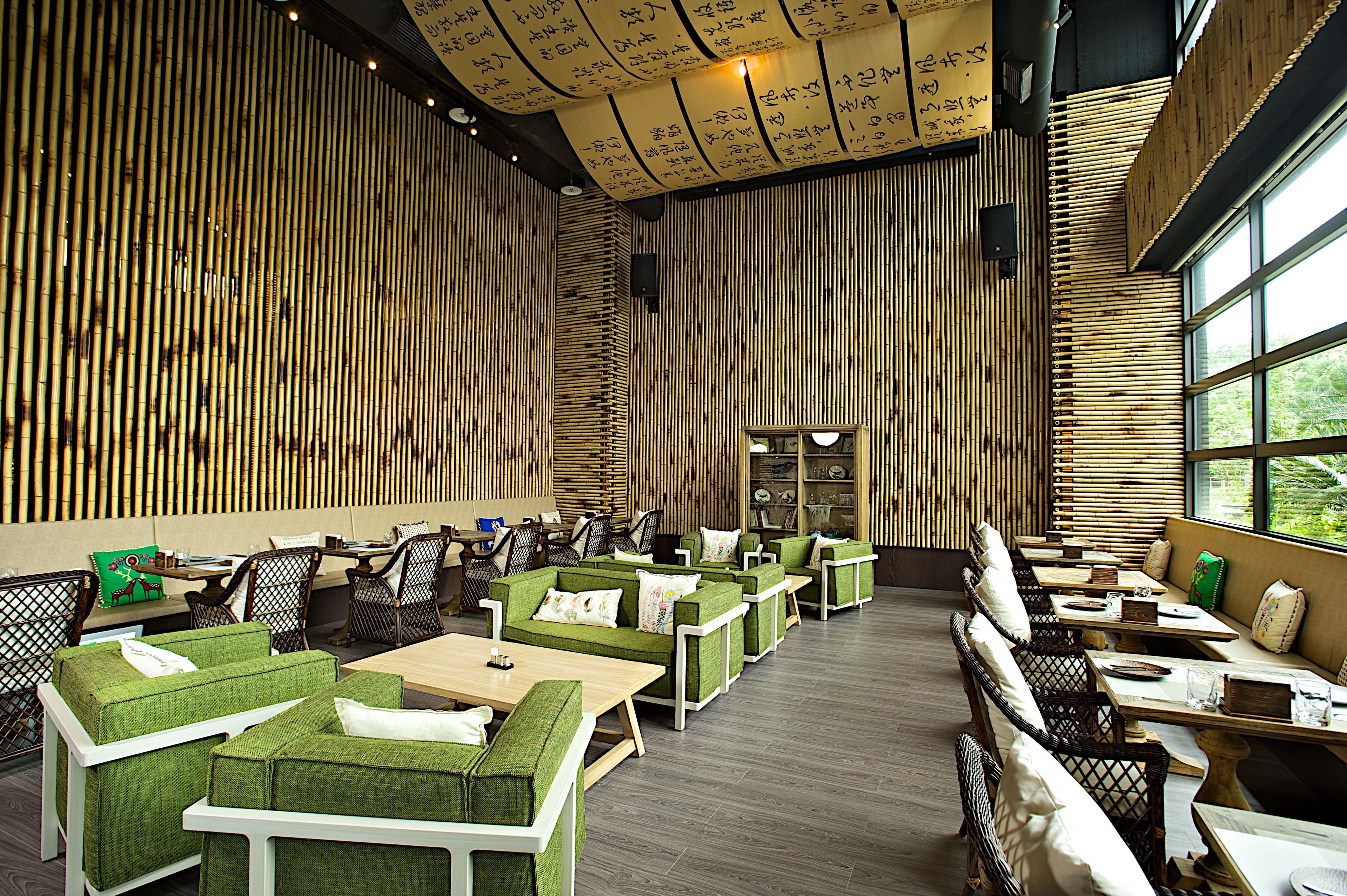 A restaurant with bamboo walls, green cushioned seating, and large windows.