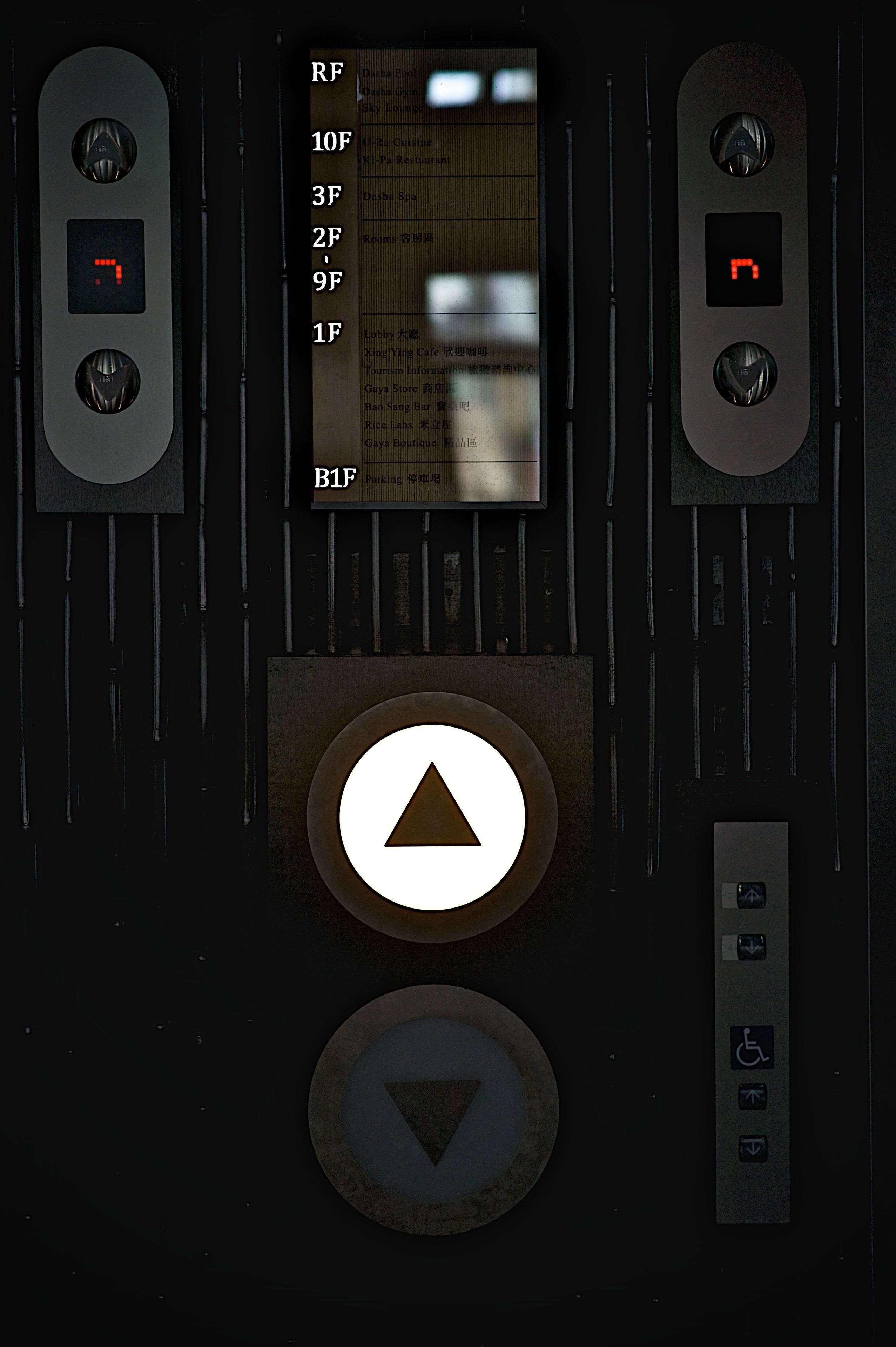 Panel de control de ascensor con botones para seleccionar pisos, una pantalla digital y botones de emergencia.
