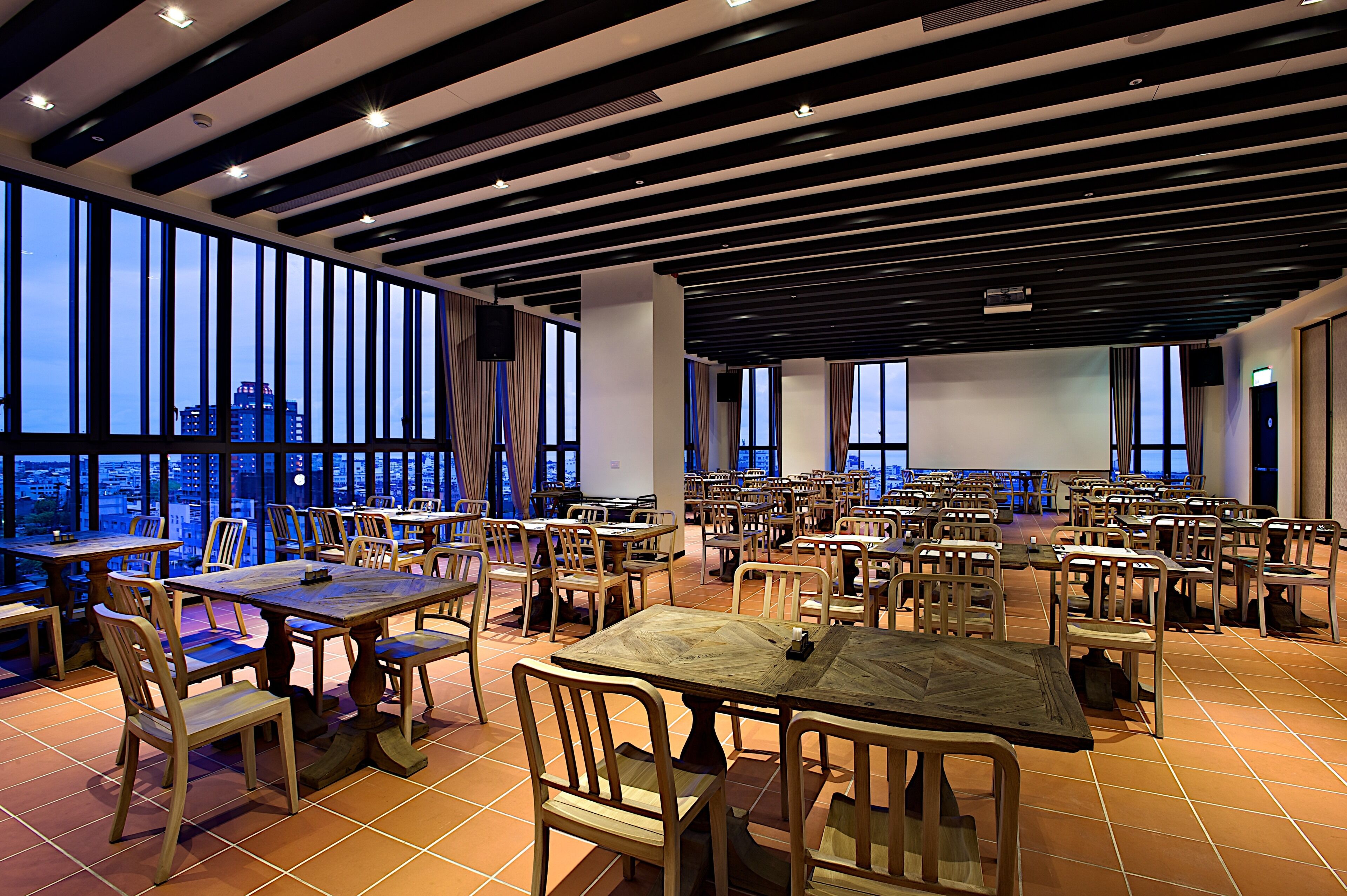 A spacious restaurant with high ceilings, large windows, and multiple dining tables and chairs.