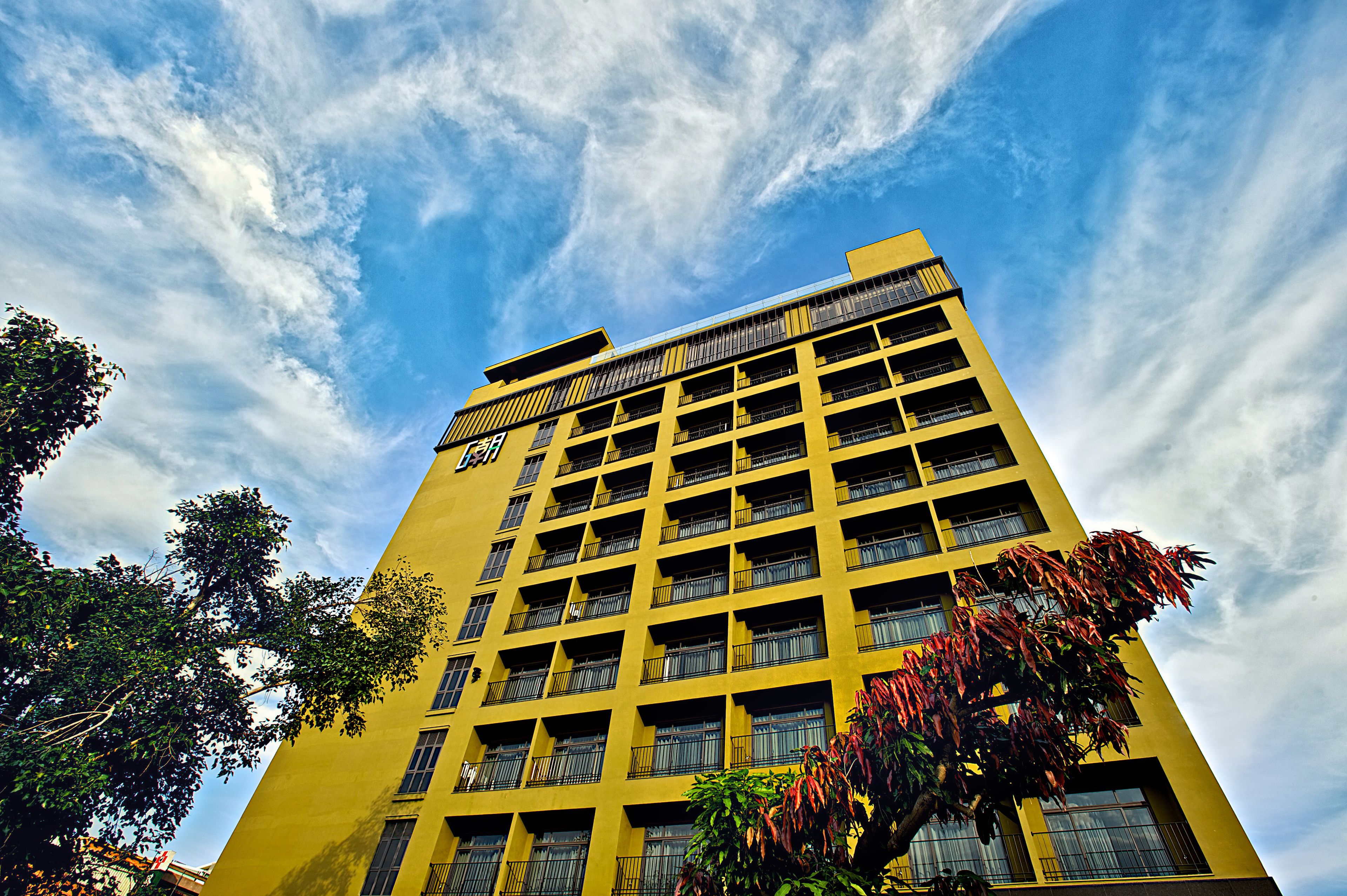 A yellow building with multiple floors and balconies, surrounded by trees.
