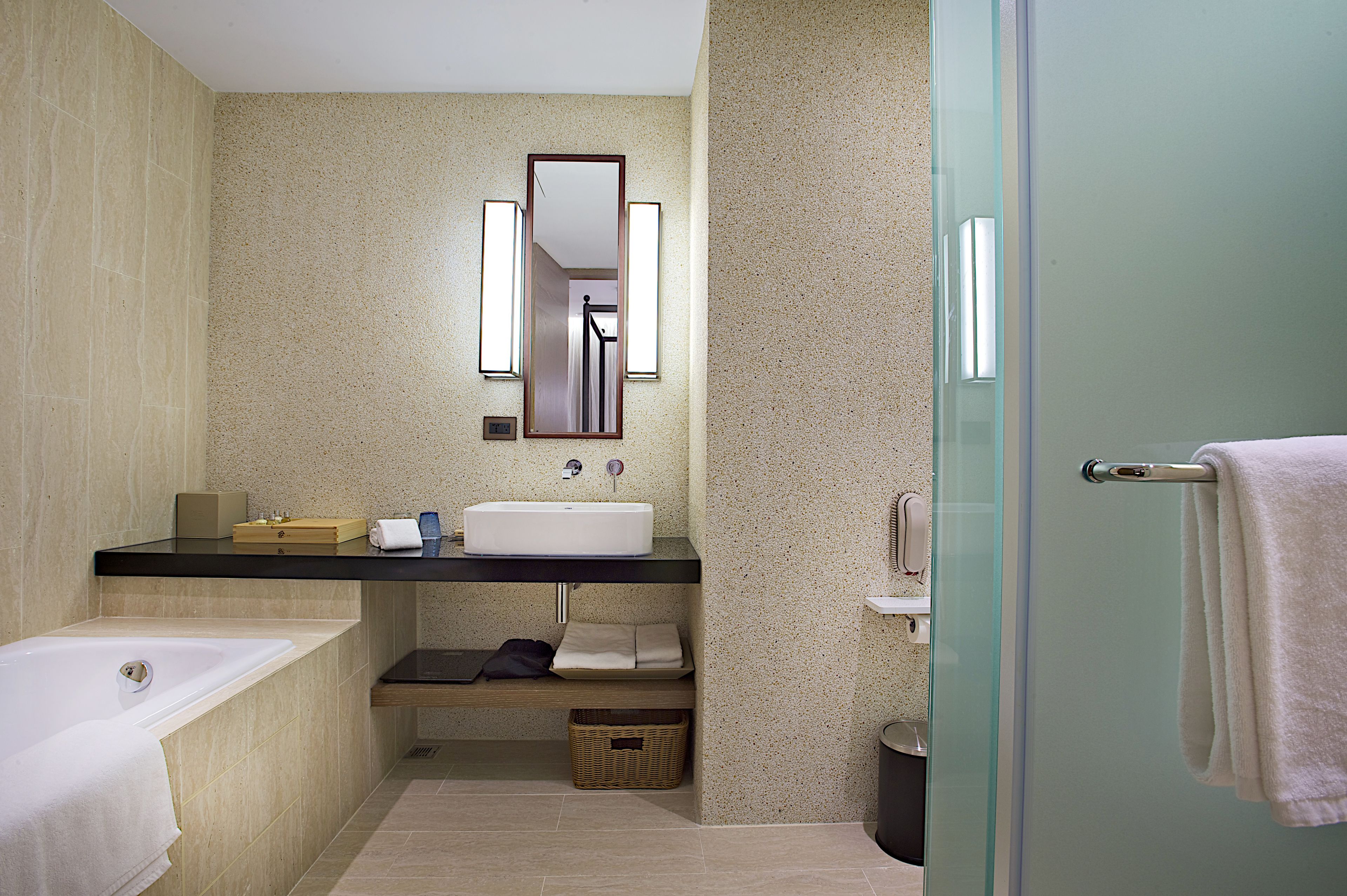 A modern bathroom with a bathtub, a sink, and a mirror. There is a towel rack and a basket.