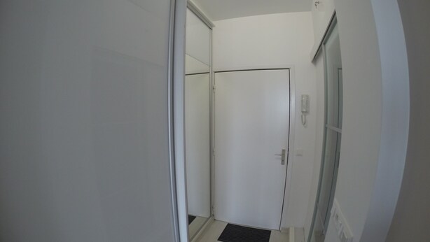Un couloir étroit avec une porte blanche, un téléphone fixé au mur et un paillasson noir devant l’entrée de la porte.