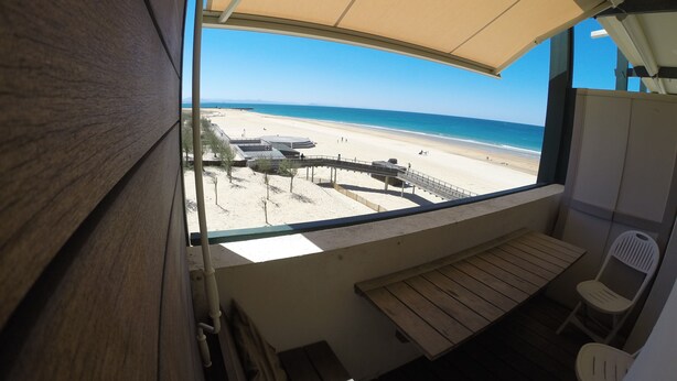 A beach view from a balcony with a wooden bench and chairs, a covered area, and a clear sky. - Magnificent ocean view studio (Soorts-Hossegor)