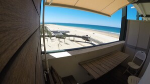 Une vue sur la plage depuis un balcon, avec un banc et des chaises en bois, un espace abrité et un ciel dégagé.