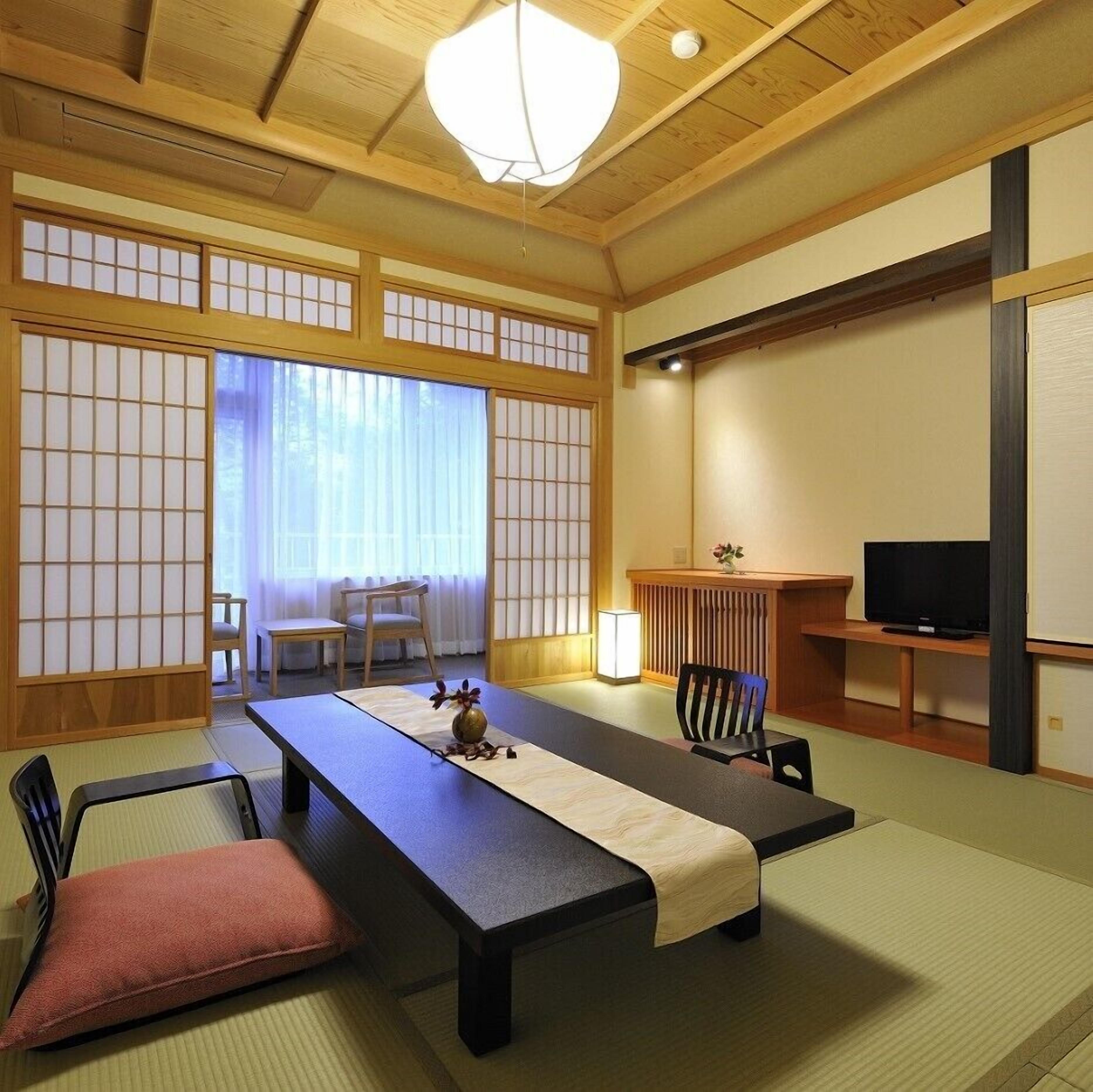 A traditional Japanese-style room with tatami flooring, a low table, chairs, a television, and sliding doors.