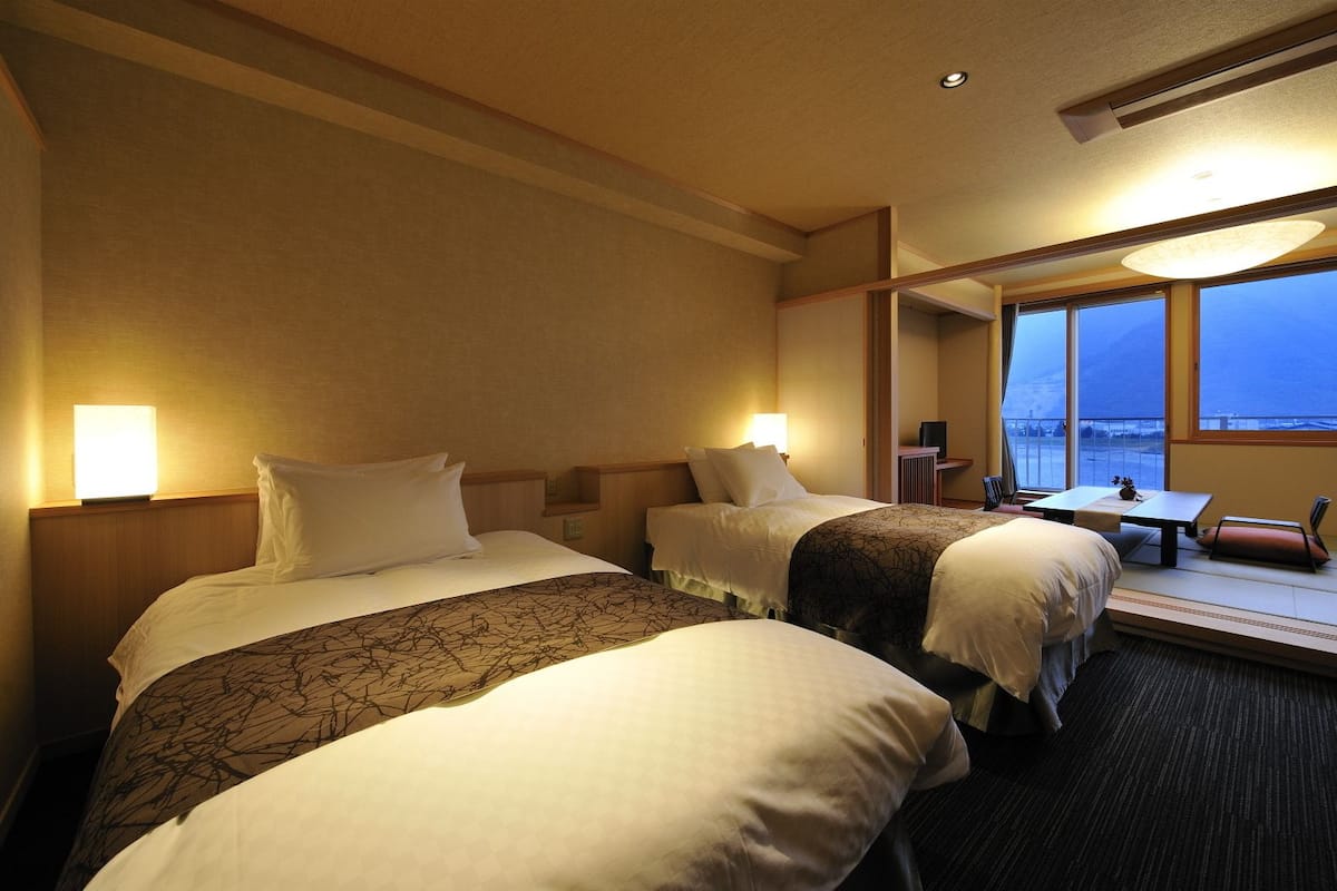 A hotel room with two beds, a desk, and a large window with a view.