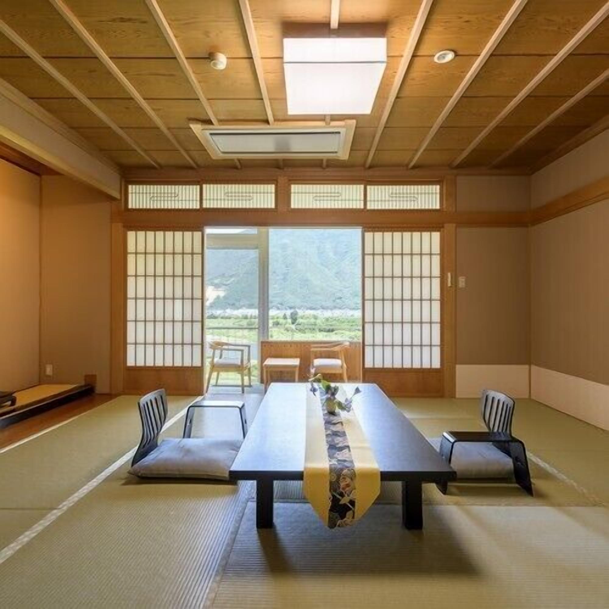 A tatami mat room with a low table, chairs, and a view of a mountainous landscape.