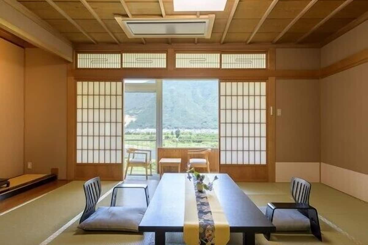 A tatami mat room with a low table, chairs, and a view of a mountainous landscape.