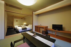 Una habitación de hotel con escritorio, dos camas, televisor y un mueble pequeño.