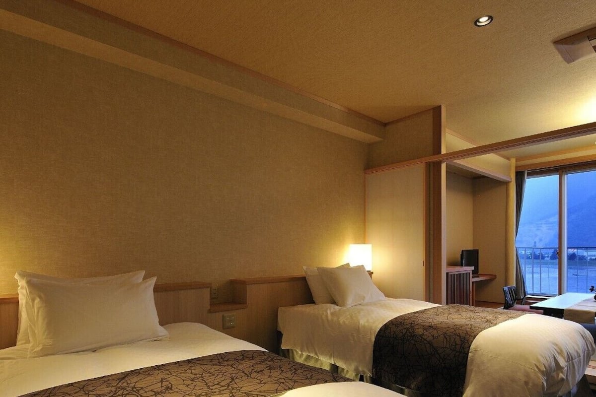 A hotel room with two beds, a desk, and a window with a view.