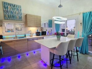 A modern kitchen with a central island, bar stools, a chandelier, and a view of the outdoors.