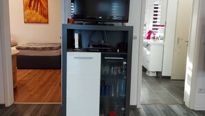 A compact living space with a TV on a stand, a small fridge, and a kitchenette area. - Beautiful apartment in Berlin-Mahlsdorf (Berlin)