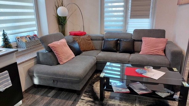 A modern living room with a grey sectional sofa, a glass coffee table, and a small side table. - Beautiful apartment in Berlin-Mahlsdorf (Berlin)