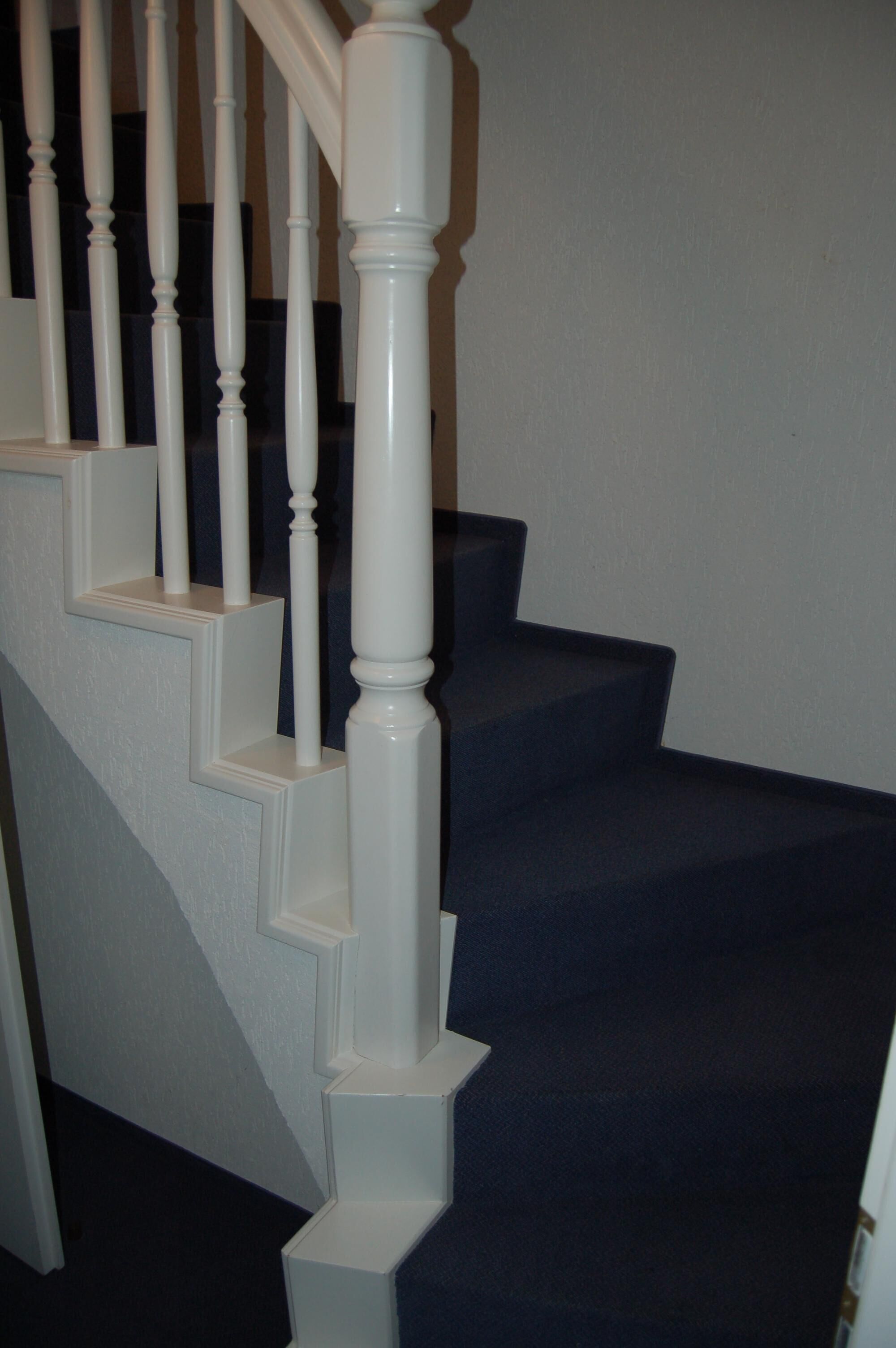 Un escalier avec des balustrades blanches et des marches recouvertes d’une moquette sombre.
