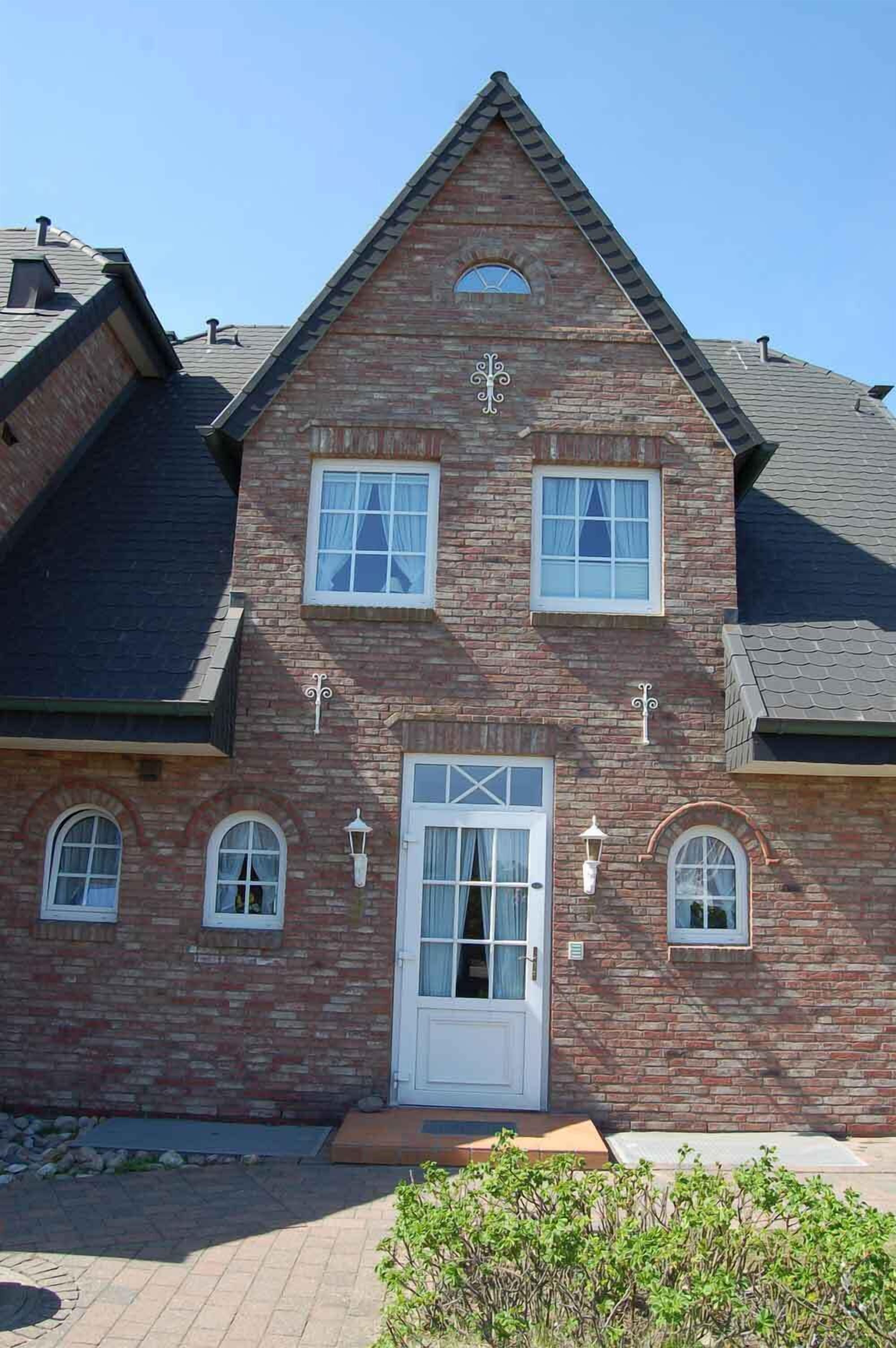 Une maison à deux étages, construite en briques, avec une porte blanche, de nombreuses fenêtres et un petit porche.