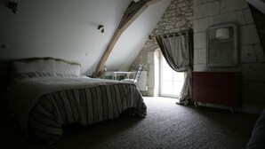 Ein Schlafzimmer mit Bett, Schminktisch, Fenster mit Vorhängen und einer Steinwand.