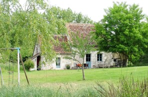 A stone house with a tiled roof, surrounded by a grassy yard and trees.
