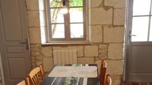 Ein Essbereich mit rustikaler Steinwand, einem Fenster mit Aussicht sowie einem Tisch mit Untersetzern und Stühlen.