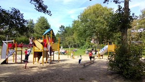 A playground with various play structures, including a slide and climbing frames, surrounded by trees and open space. - NEW .. Charming duplex T2 with pool and tennis (Neufchâtel-Hardelot)