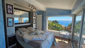 Un dormitorio con una cama grande, una mesita de noche, una silla, una ventana con vistas al mar y un espejo en la pared.