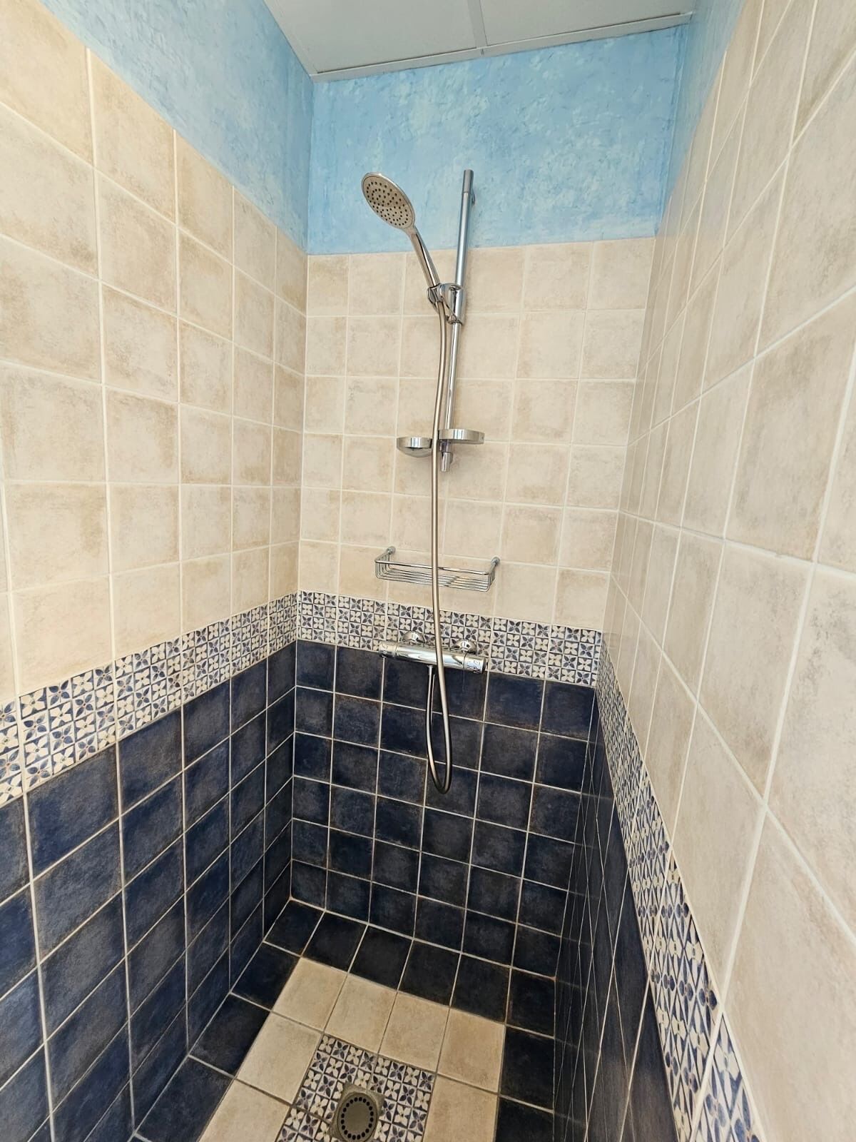 A shower with a handheld showerhead and a wall-mounted faucet.