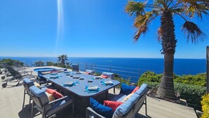 Un área de comedor al aire libre con vistas al océano, equipada con mesas y sillas.