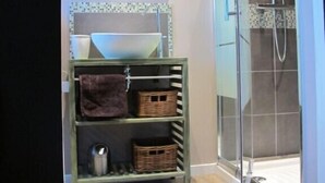 Une salle de bain avec une douche à parois de verre, un lavabo avec un miroir au-dessus et une étagère avec des paniers et des serviettes.
