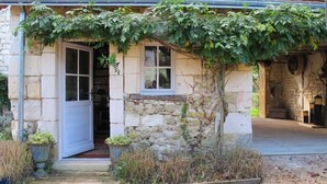 Un bâtiment en pierre avec une porte et des fenêtres blanches, un porche en bois et un mur couvert de lierre.