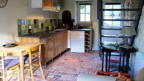Une cuisine avec un sol en briques, des armoires en bois, une table à manger avec des chaises, une fenêtre et un luminaire suspendu.