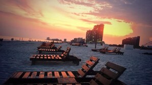 A beach with wooden lounge chairs and a city skyline in the background.