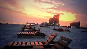 Una playa con sillones de madera y un horizonte urbano al fondo.