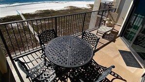 A balcony with a round table and chairs, overlooking a beach with white sand and the ocean.