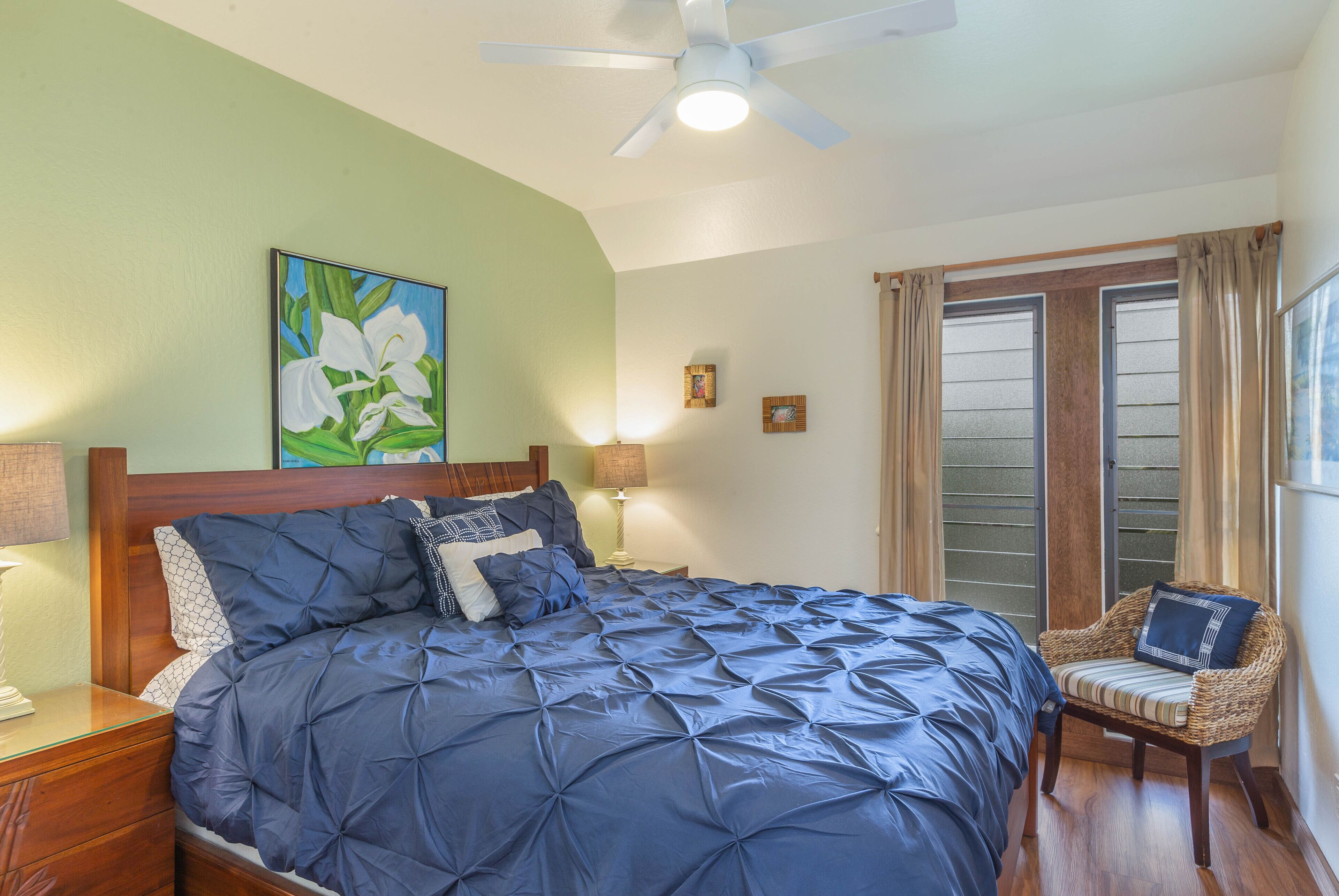 A bedroom with a large bed, a wooden headboard, a ceiling fan, and a window with curtains.