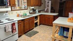A kitchen with wooden cabinets, a white countertop, a stove, and a sink. - Only 1 dollar cleaning fee at Pictured Rocks Basecamp on the Manistique River! (Germfask)