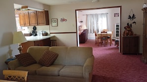 A living room with a sofa, a dining area with a table and chairs, and a kitchen with cabinets and a countertop. - Only 1 dollar cleaning fee at Pictured Rocks Basecamp on the Manistique River! (Germfask)